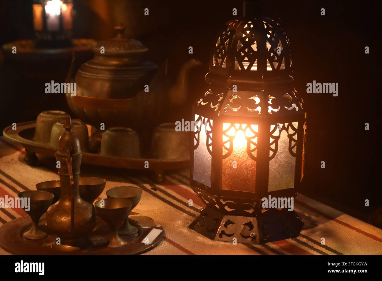 Lamps arabi che emettono luce con teiera e tazza sul tavolo nel buio Foto Stock