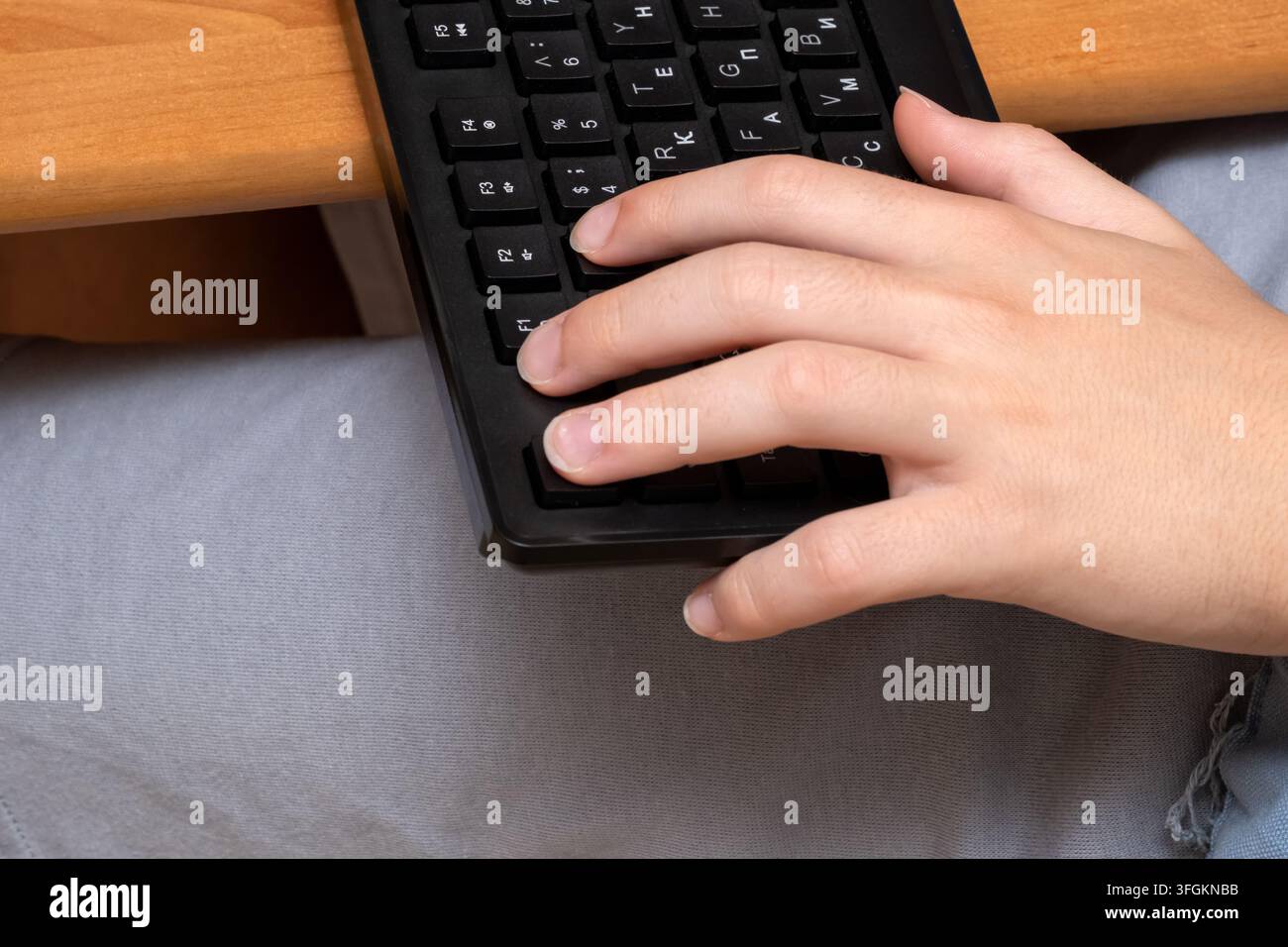 Un primo piano di una persona caucasica che digita a mano su una tastiera di computer nera a una scrivania di legno Foto Stock