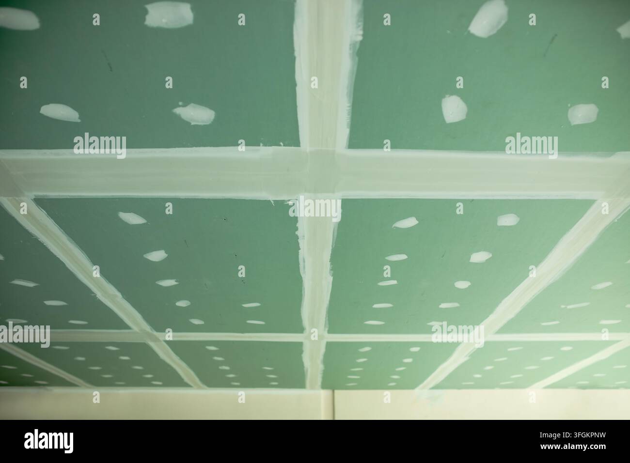 Soffitto in cartongesso verde mostra giunzioni incollato che si incrociano al centro, fossette di viti rattoppate punteggiano la superficie in un modello sparso, finitura a secco wo Foto Stock