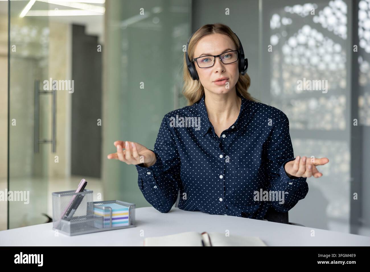 Comunicazione remota e riunione virtuale, donna professionista con auricolari che parla alla telecamera durante una videochiamata in ufficio. Foto Stock