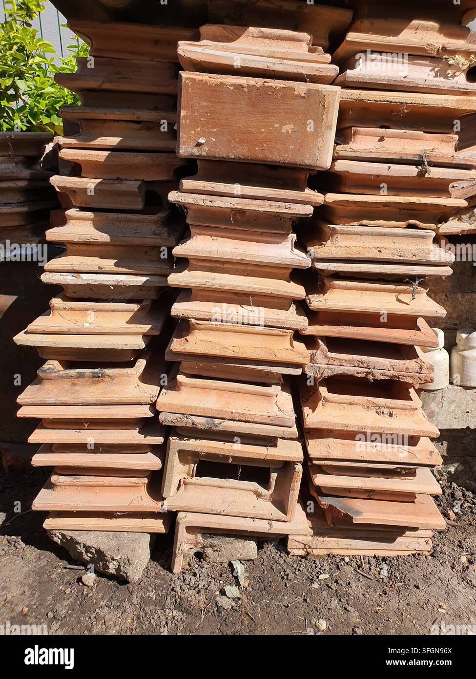 Una vista ravvicinata di numerose tegole di terracotta consumate impilate in file verticali contro un muro di cemento ruvido. Le tegole di argilla mostrano varie Foto Stock