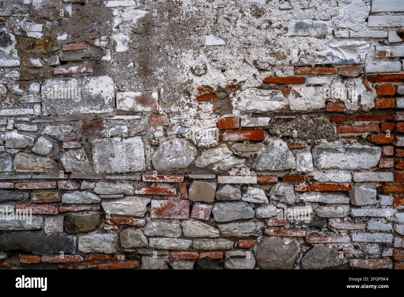 Vista ravvicinata di un muro di muratura invecchiato che combina pietre irregolari, mattoni rossi e malta, con superfici consumate e texture variate su tutta la struttura. Foto Stock