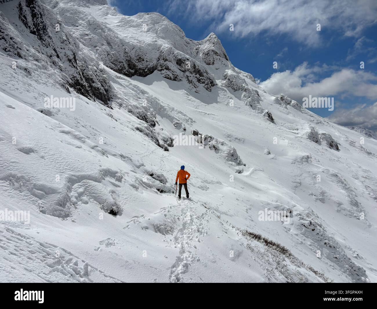 Alpinista con piccozza da ghiaccio in piedi su un ripido pendio nevato sotto la vetta innevata del Reichenstein durante una spedizione di arrampicata invernale ad alta quota a Eise Foto Stock