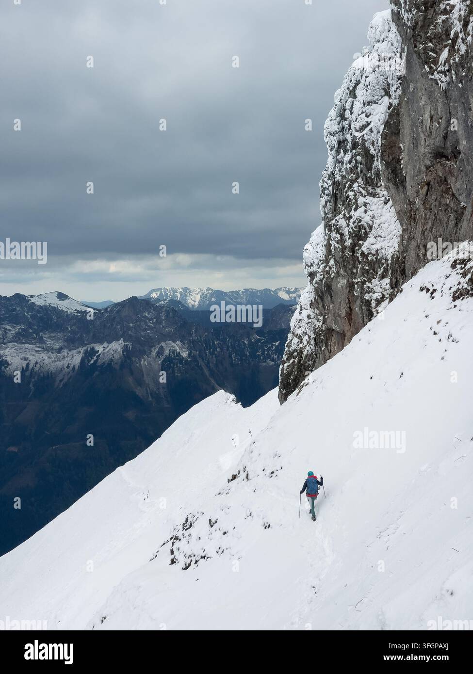 Alpinista che scende un ripido pendio innevato accanto a una scogliera rocciosa sulla vetta del monte Reichenstein durante una spedizione di arrampicata invernale ad alta quota a Eis Foto Stock