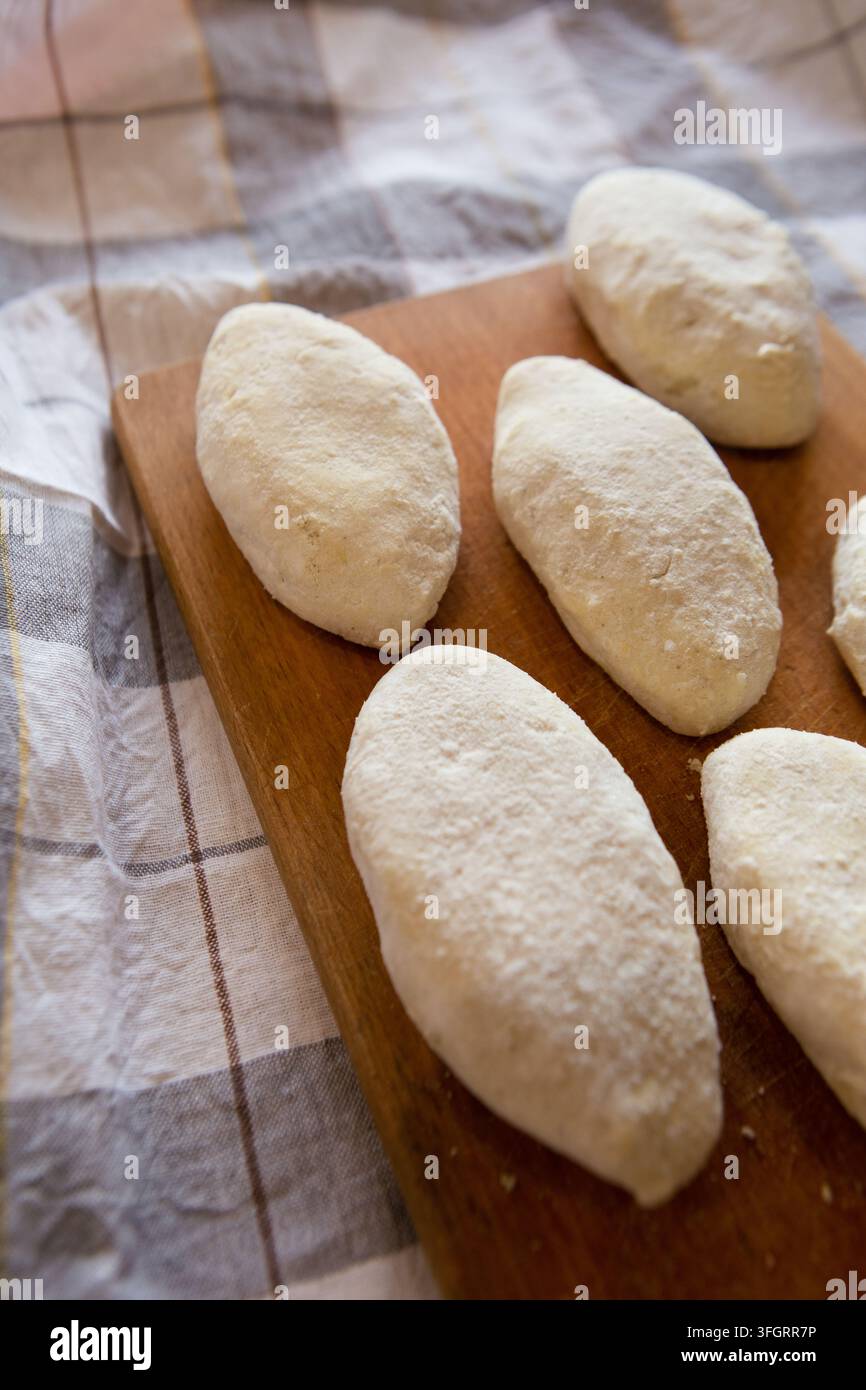 I panini di pasta lievitata sono posizionati su una tavola di legno pronti per essere cotti. La cucina ha una tovaglia a scacchi sotto la tavola. Il momento è probabilmente durante la mattina Foto Stock