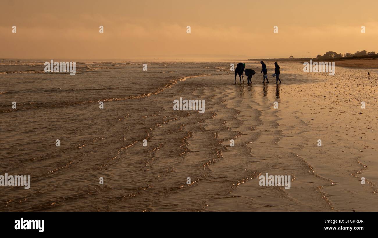 Una famiglia che si gode il tempo sulla spiaggia in silhouette al tramonto Foto Stock