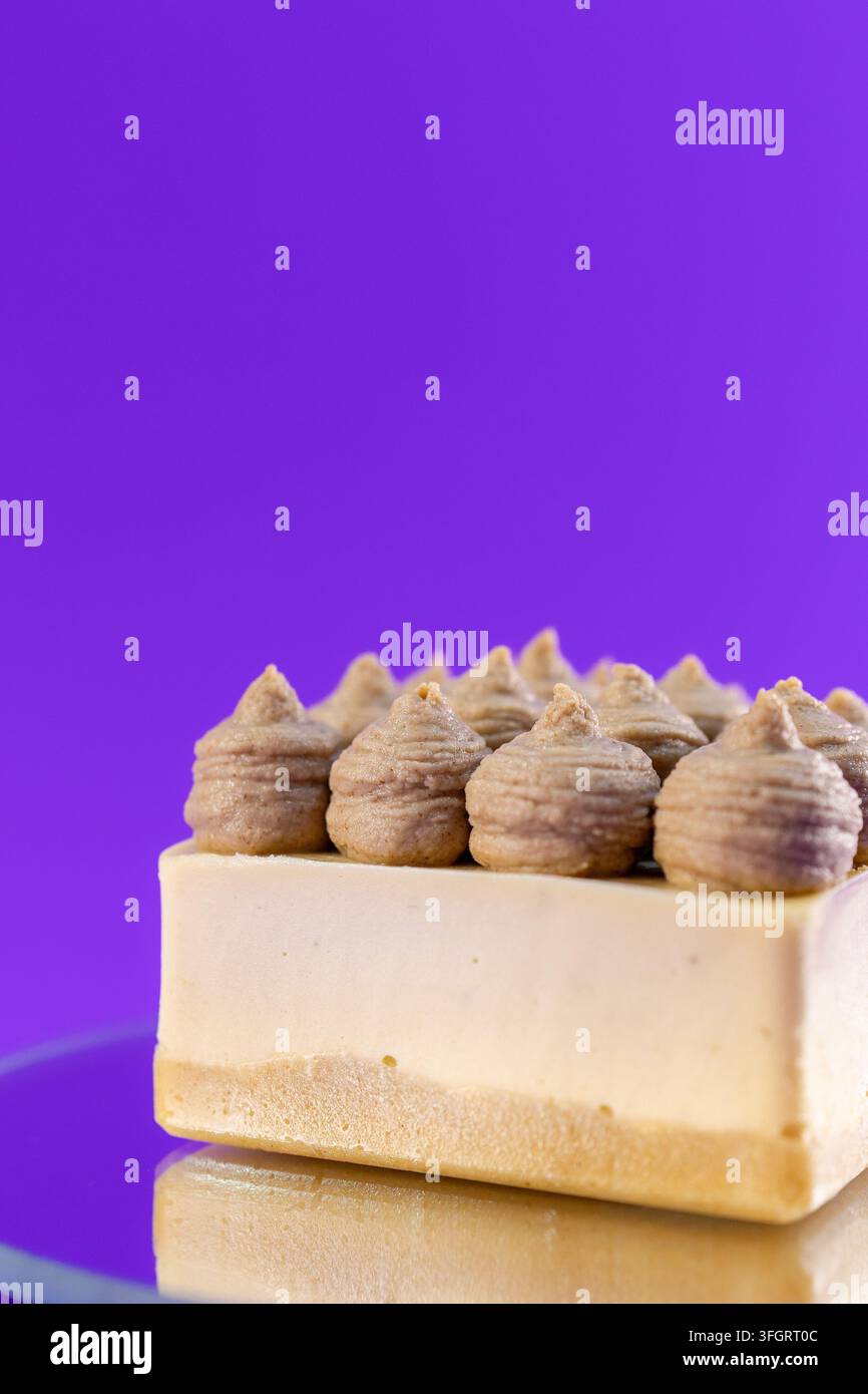 Un dolce è esposto su un piatto di vetro contro uno sfondo viola vivace. Il dolce ha strati lisci e piccole punte di glassa in superficie, che mostrano cura Foto Stock
