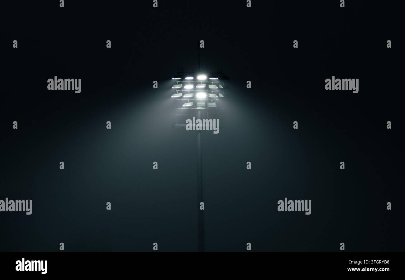 un alto palo dell'illuminazione dello stadio dotato di più file di lampade LED ad alta intensità o al metallo alogeno che attraversa una notte nebbiosa Foto Stock