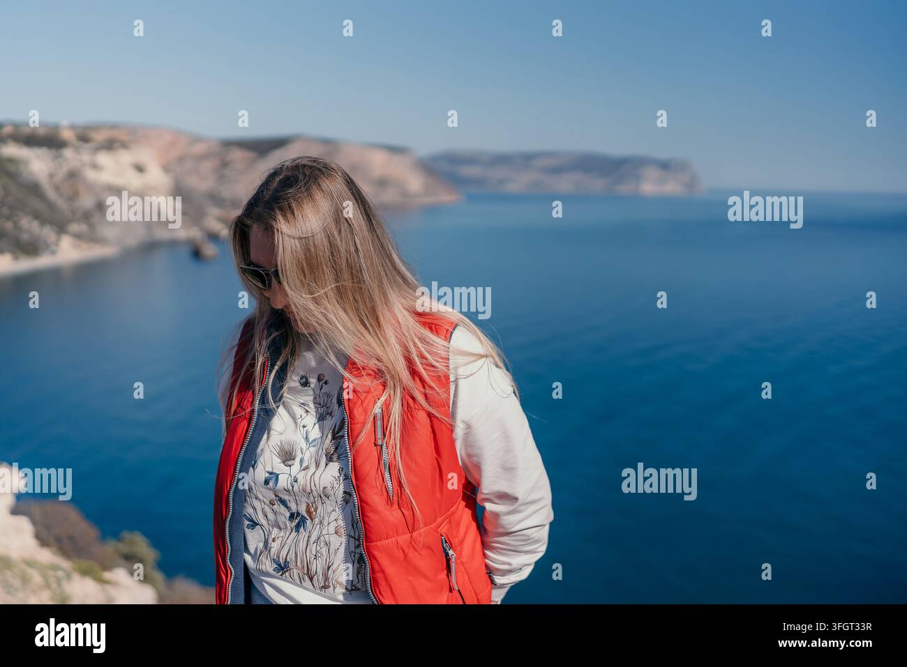 Donna in viaggio costiero in piedi sul bordo di una scogliera che si affaccia sull'oceano blu e sulle montagne rocciose in una giornata di sole Foto Stock