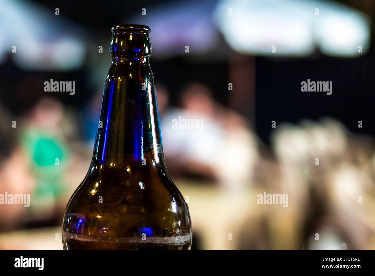 Un piano a fuoco selettivo del collo e della parte superiore di una bottiglia di bevanda in vetro marrone in un mercato notturno all'aperto o in un pub, con uno splendido sfondo sfocato Foto Stock