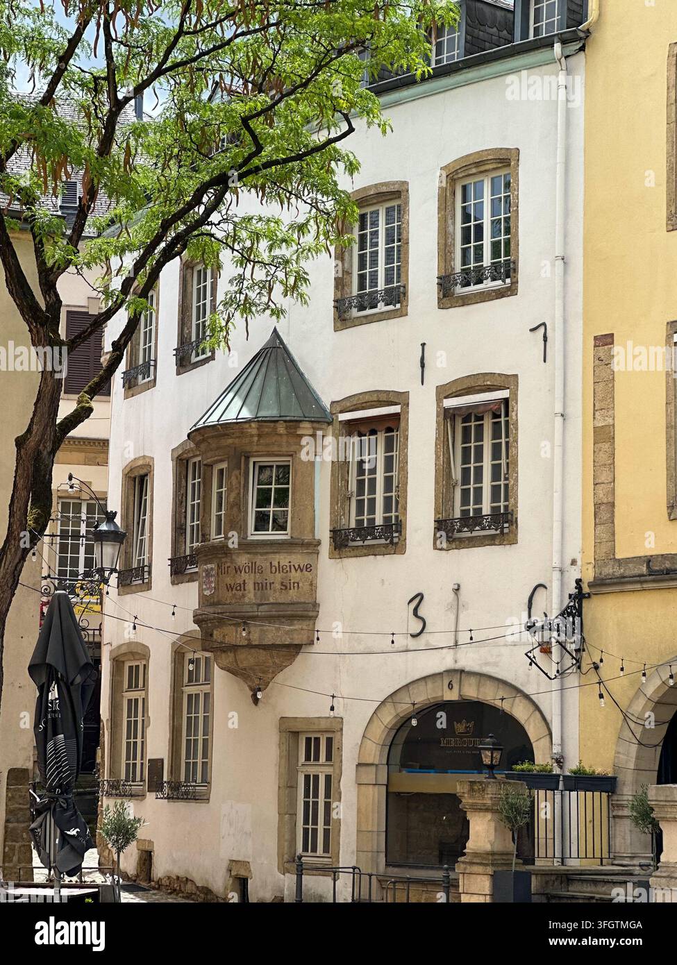 Edificio bianco storico europeo con una finestra a bovindo d'angolo e ingresso ad arco. Tradizionale casa di città bianca europea con grata ornata di pietra. - Immagine stock catturata con smartphone
