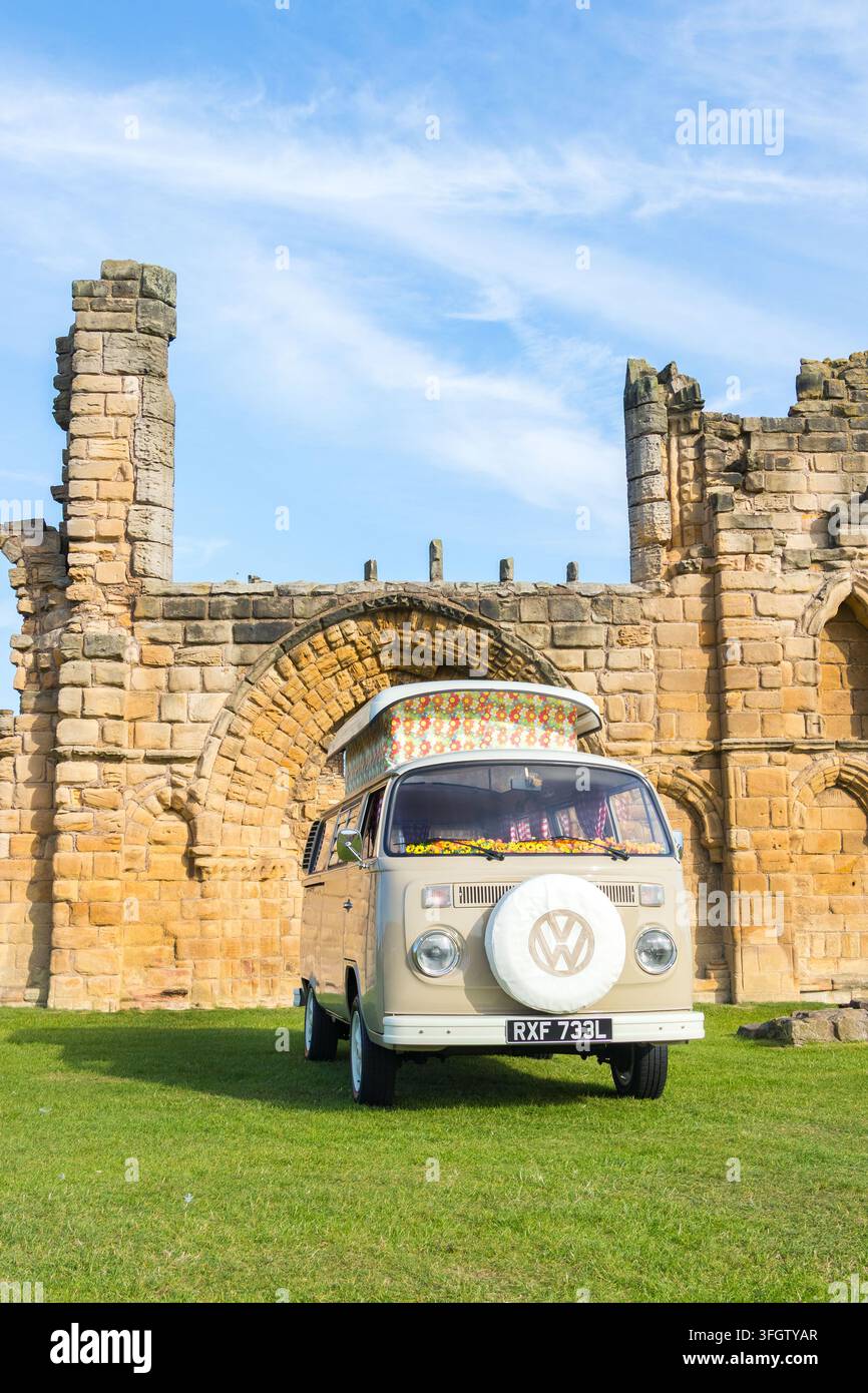 Un camper vintage beige Volkswagen Type 2 parcheggiato sull'erba davanti alle rovine del priorato in pietra di Tynemouth Foto Stock