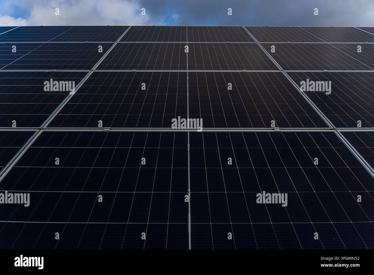 Array di pannelli solari con celle fotovoltaiche scure sotto un cielo parzialmente nuvoloso. Foto di alta qualità Foto Stock