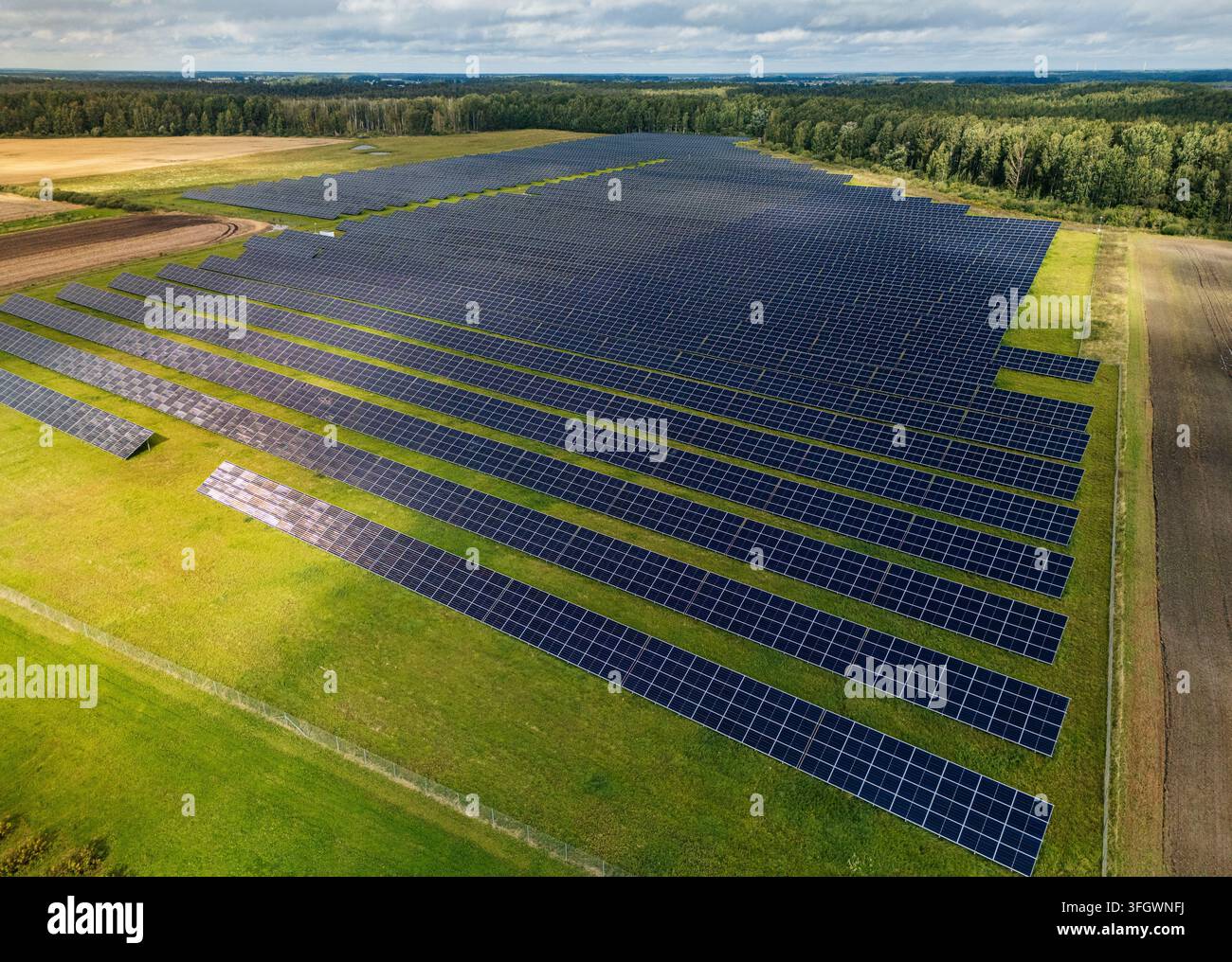 Vista aerea di una grande fattoria solare con file di pannelli fotovoltaici su una campagna verde circondata da foreste e terreni agricoli, energia rinnovabile rurale e così Foto Stock