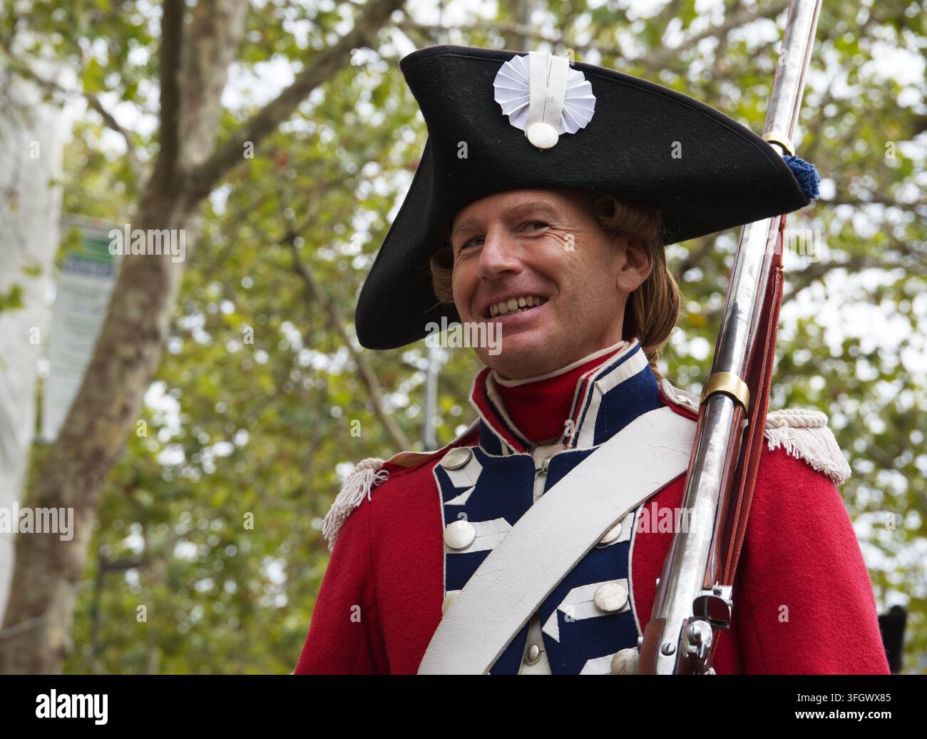 Un rievocatore storico sorridente in uniforme militare del XVIII secolo e tricorno che tiene un moschetto durante una parata a Parigi, Francia. Foto Stock