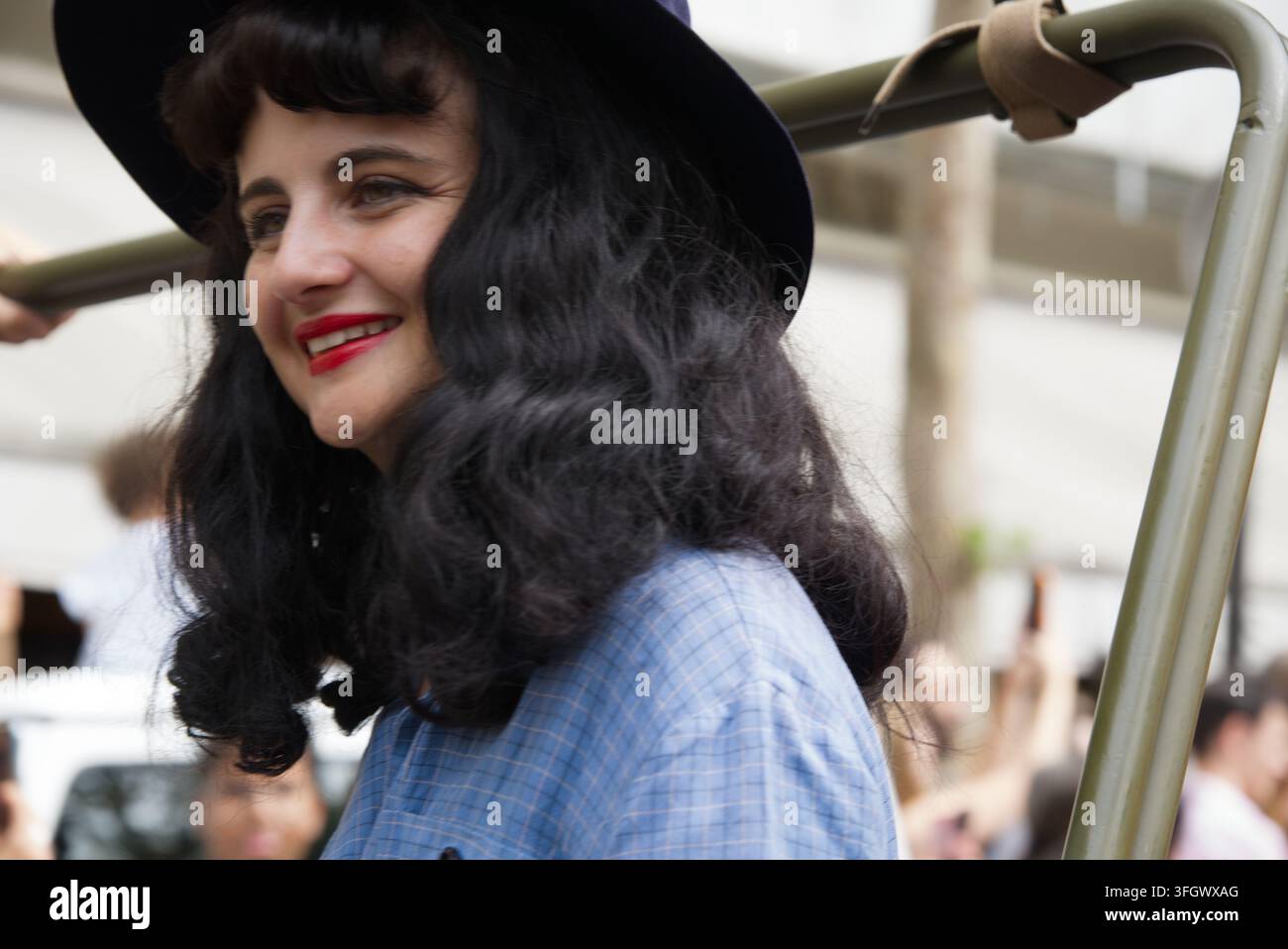 Una donna con un’acconciatura victory rolls anni '40 e rossetto rosso a bordo di un veicolo militare d’epoca durante una parata di strada a Parigi, Francia. Foto Stock
