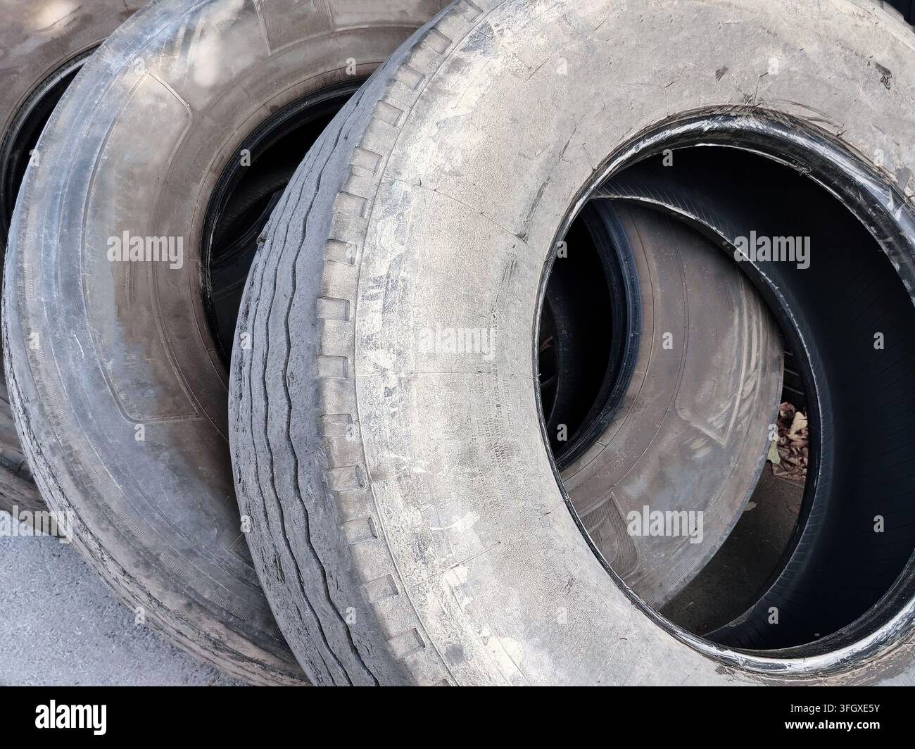 Gomme usate accatastate e inclinate esposte all'aperto contro un muro ondulato scuro, che mostrano diversi modelli di battistrada, dimensioni, superfici consumate e gravità Foto Stock