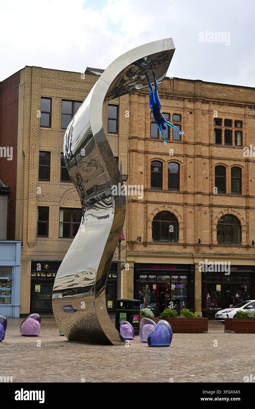 Scultura riflettente con figura blu sospesa in una piazza urbana moderna Foto Stock