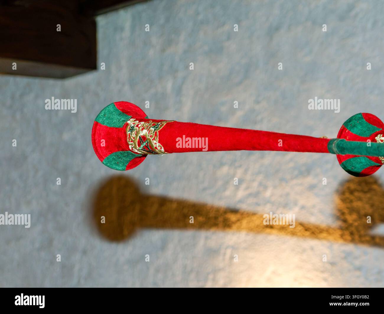 Barriera in corda di velluto rosso con finitura dorata decorativa che proietta un'ombra su una parete interna Foto Stock