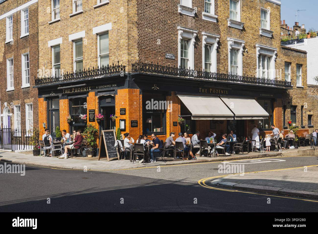 I clienti riempiono i tavoli sul marciapiede fuori dal pub The Phoenix in un angolo soleggiato di Chelsea, Londra, Inghilterra, Regno Unito Foto Stock
