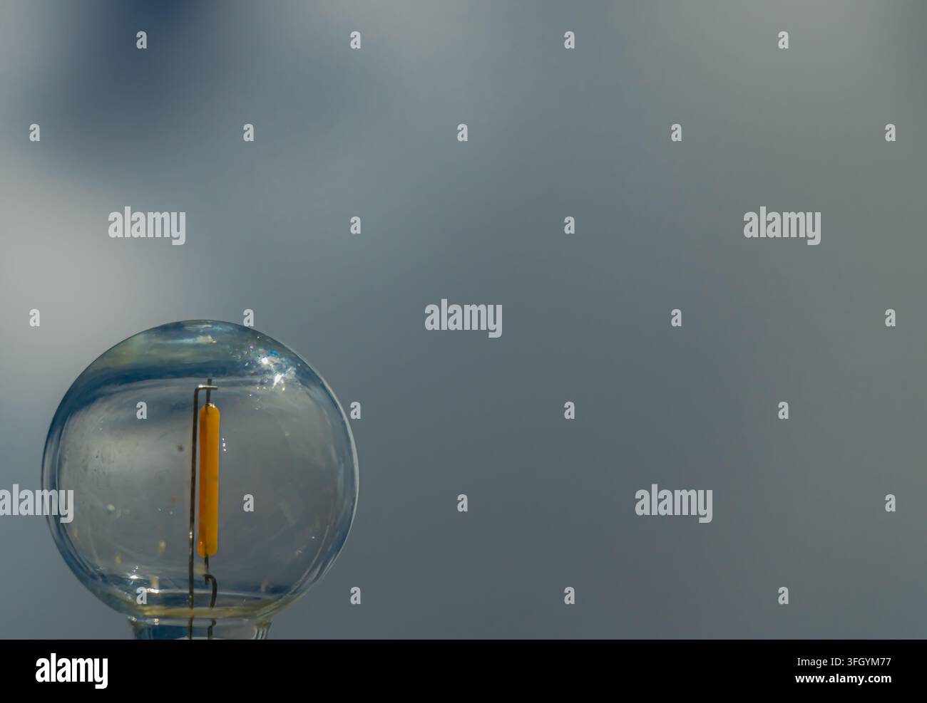 Prima vista di una lampadina a filamento LED trasparente con striscia luminosa gialla su uno sfondo grigio morbido, lasciando ampio spazio per il testo su energia e illuminazione Foto Stock