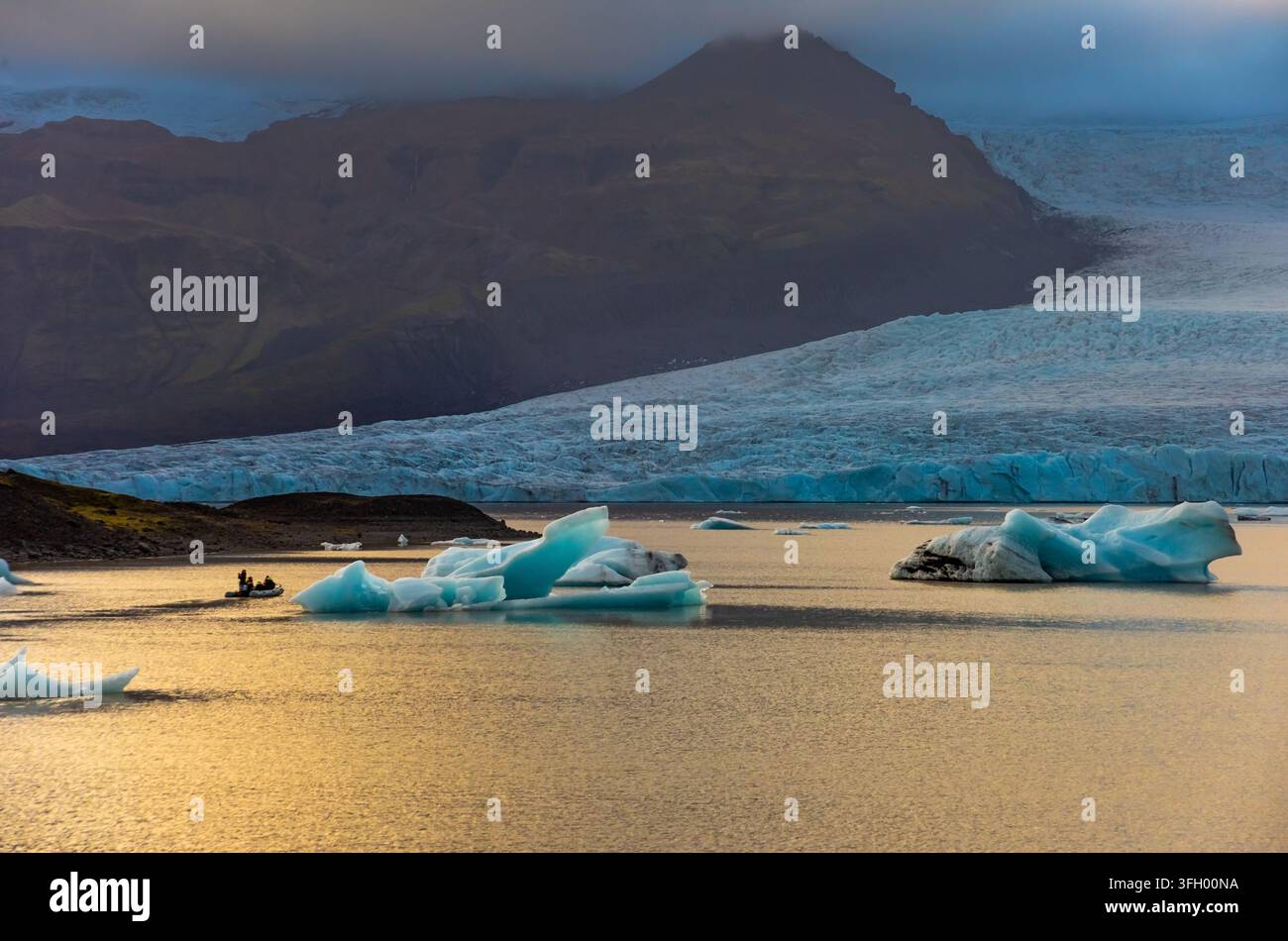 La laguna glaciale di Fjallsarlon presenta iceberg che galleggiano in acque calme, riflettendo il soffice bagliore del crepuscolo sullo sfondo del massiccio ghiacciaio. An Foto Stock