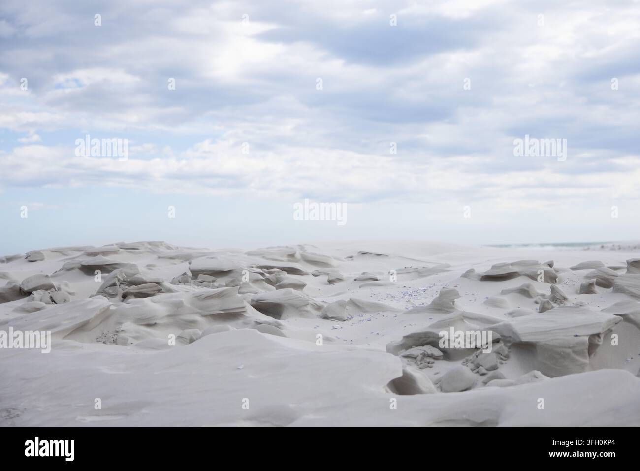 Rocce modellate dal vento formano pianure di sabbia costiera con ciotoli e cavità poco profonde sotto un cielo nuvoloso Foto Stock