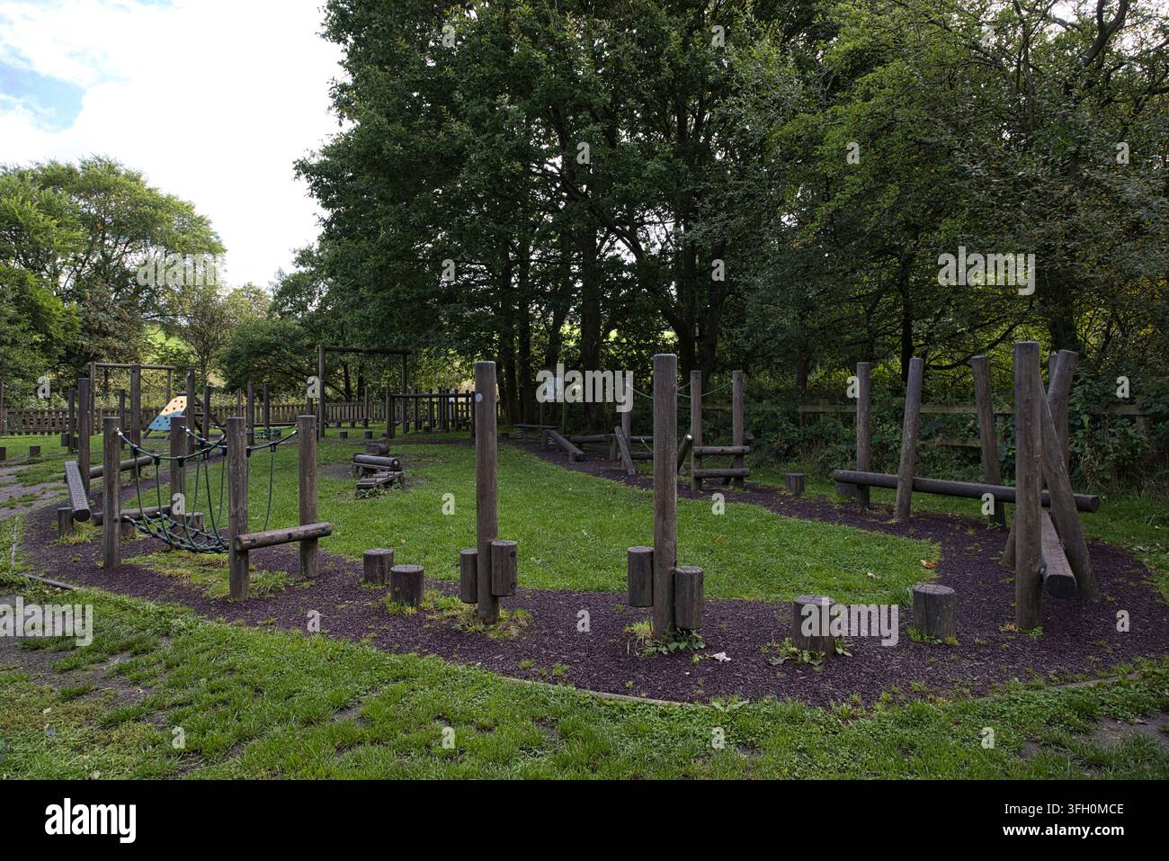 Attrezzature da gioco in legno per esterni e percorso a ostacoli su una radura erbosa circondata da alberi. Foto Stock