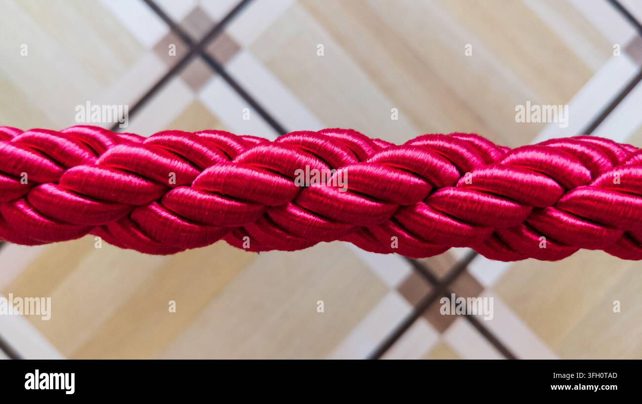 Corda in velluto rosso spesso intrecciato utilizzata per barriere di staccionata nei musei. Posizionata orizzontalmente su uno sfondo interno di parquet geometrico in legno Foto Stock