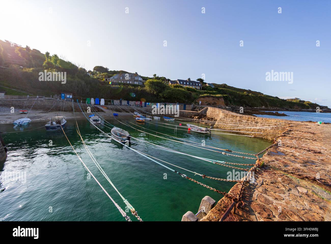 Una vista ad angolo basso da una riva rocciosa, che mostra diverse piccole barche ormeggiate in acque chiare e blu-verdi, con la costa frastagliata e la massa terrestre lontana Foto Stock