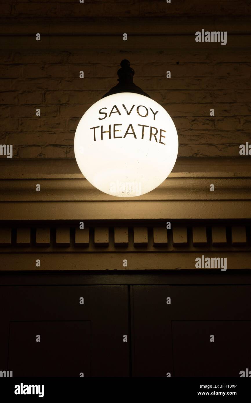 Un'insegna a forma di globo luminosa illumina la notte per segnalare l'ingresso del teatro storico Savoy a Londra, in Inghilterra, accogliendo i visitatori. Foto Stock