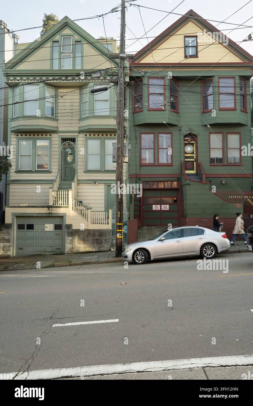 I pedoni passano davanti a un'auto parcheggiata su una strada di San Francisco per recarsi al lavoro oltre due case ornate in stile vittoriano. Foto Stock