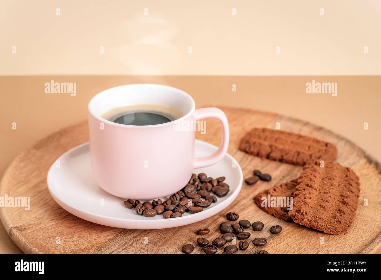 Tazza da caffè rosa con piattino, chicchi di caffè e biscotti disposti su una tavola di legno in un ambiente caldo e accogliente, primo piano. Foto Stock