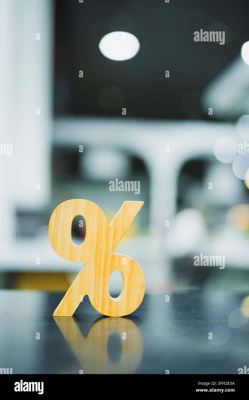 Insegna di sconto in percentuale in legno su tavolo riflettente con sfondo sfocato bokeh, rappresentante tasso di interesse bancario, rapporto fiscale finanziario, vendita al dettaglio Foto Stock