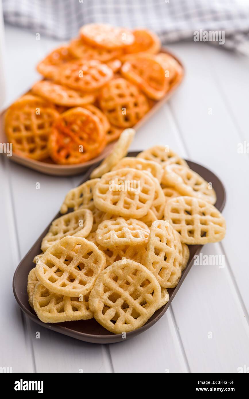 Due ciotole di snack di patate waffle presentate fianco a fianco, uno speziato e l'altro salato classico. Patatine croccanti e dorate su un tavolo luminoso evocano ca Foto Stock