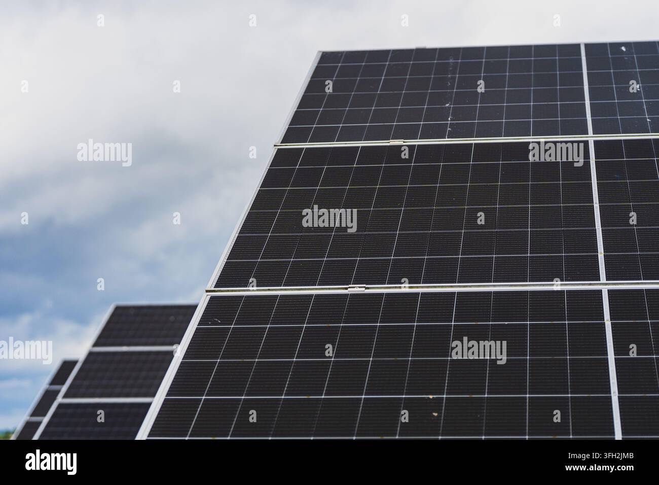 Prima piano a bassa angolazione di pannelli solari fotovoltaici con celle scure e cornici argentate contro un cielo parzialmente nuvoloso. Foto di alta qualità Foto Stock