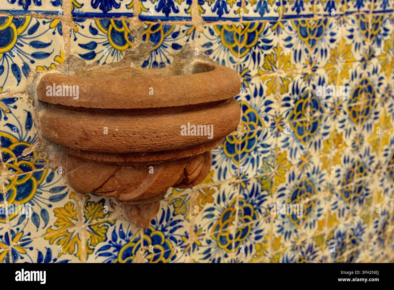 Vista di un bacino in pietra di terracotta montato su una parete rivestita con tradizionali piastrelle azulejo blu e gialle all'interno dell'Igreja Matriz de Santiago do Cace Foto Stock
