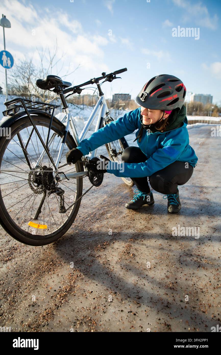 Una donna di mezza età controlla la catena della sua bicicletta su una strada ghiacciata a Helsinki, in Finlandia, dimostrando la manutenzione invernale della bicicletta e la riparazione della bici. Foto Stock