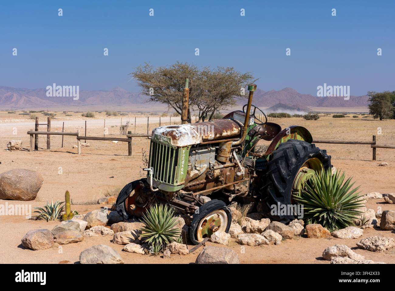 Trattore Ferguson vintage in un paesaggio rurale arido vicino a Opuwo, regione di Kunene, Namibia, con montagne, alberi di acacia e piante del deserto. Foto Stock