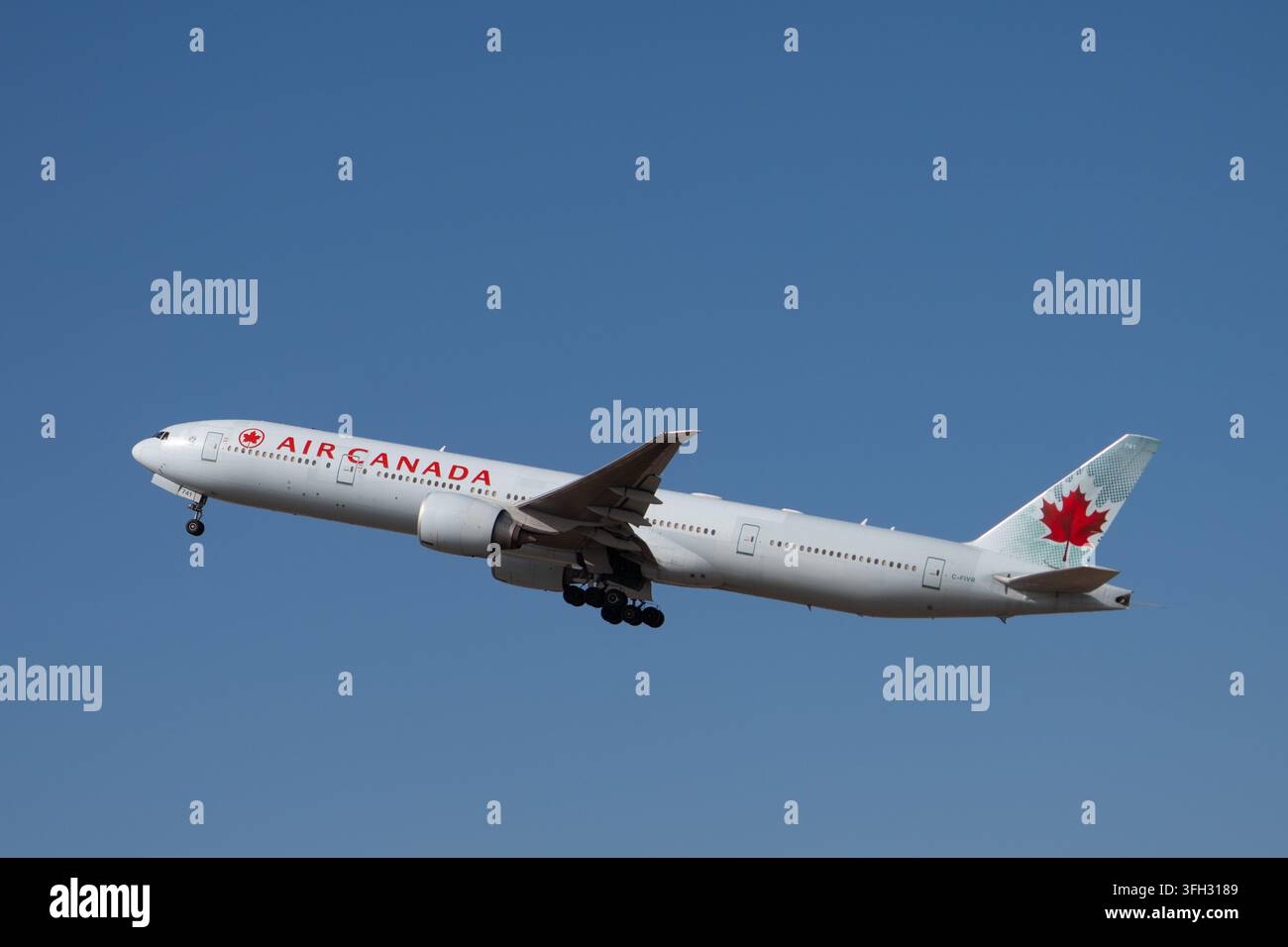 Jet passeggeri a fusoliera larga Boeing 777 di Air Canada che si eleva in un cielo blu chiaro dopo il decollo con il carrello di atterraggio esteso. Foto Stock