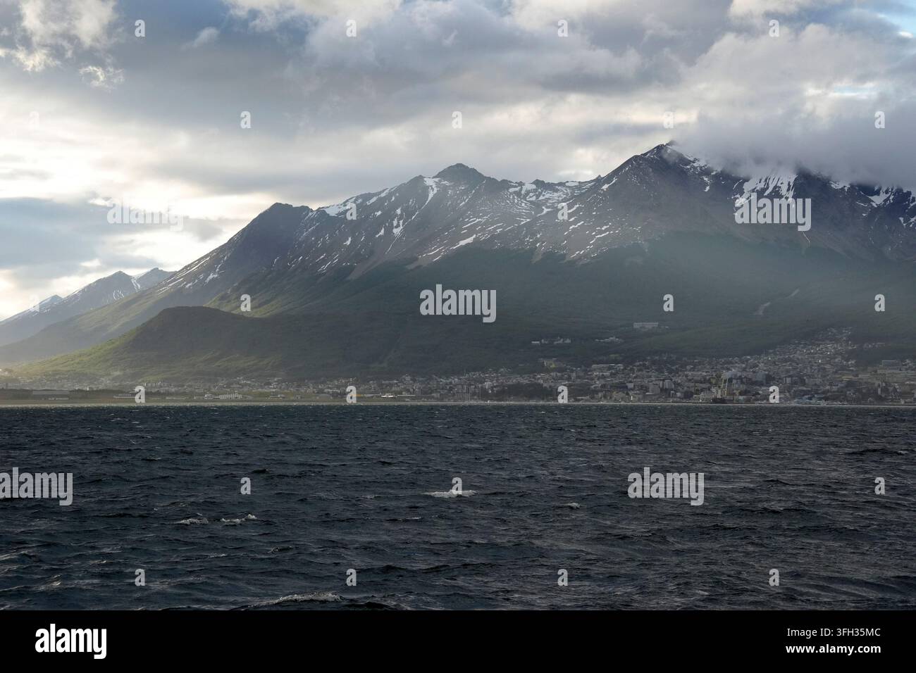 Vista panoramica di Ushuaia, Argentina, dal Canale di Beagle con le drammatiche montagne innevate di Martial e cieli tempestosi. Foto Stock