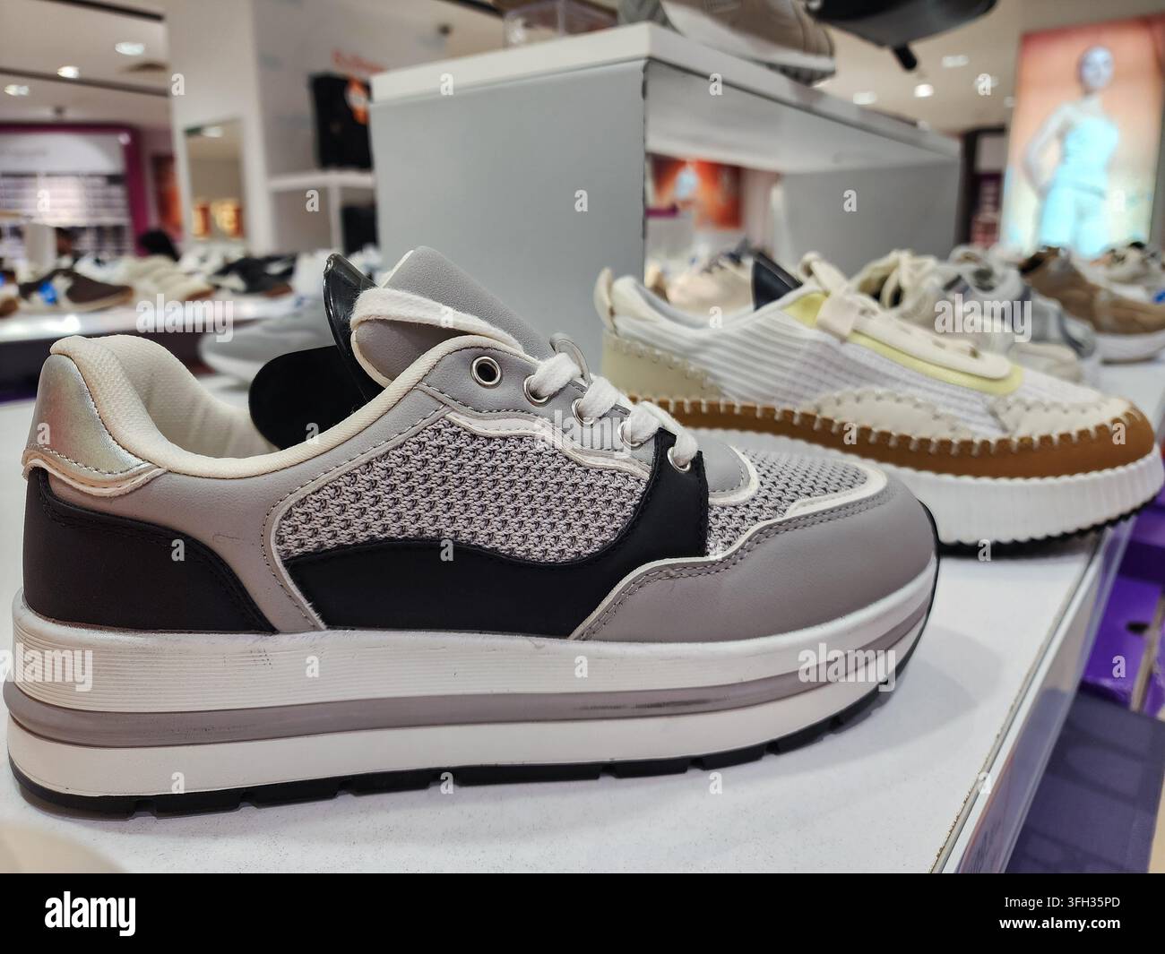 Sneakers e scarpe con plateau sono esposti su uno scaffale bianco all'interno di un moderno negozio al dettaglio di calzature, evidenziando le tendenze attuali della moda e l'interesse dei consumatori Foto Stock