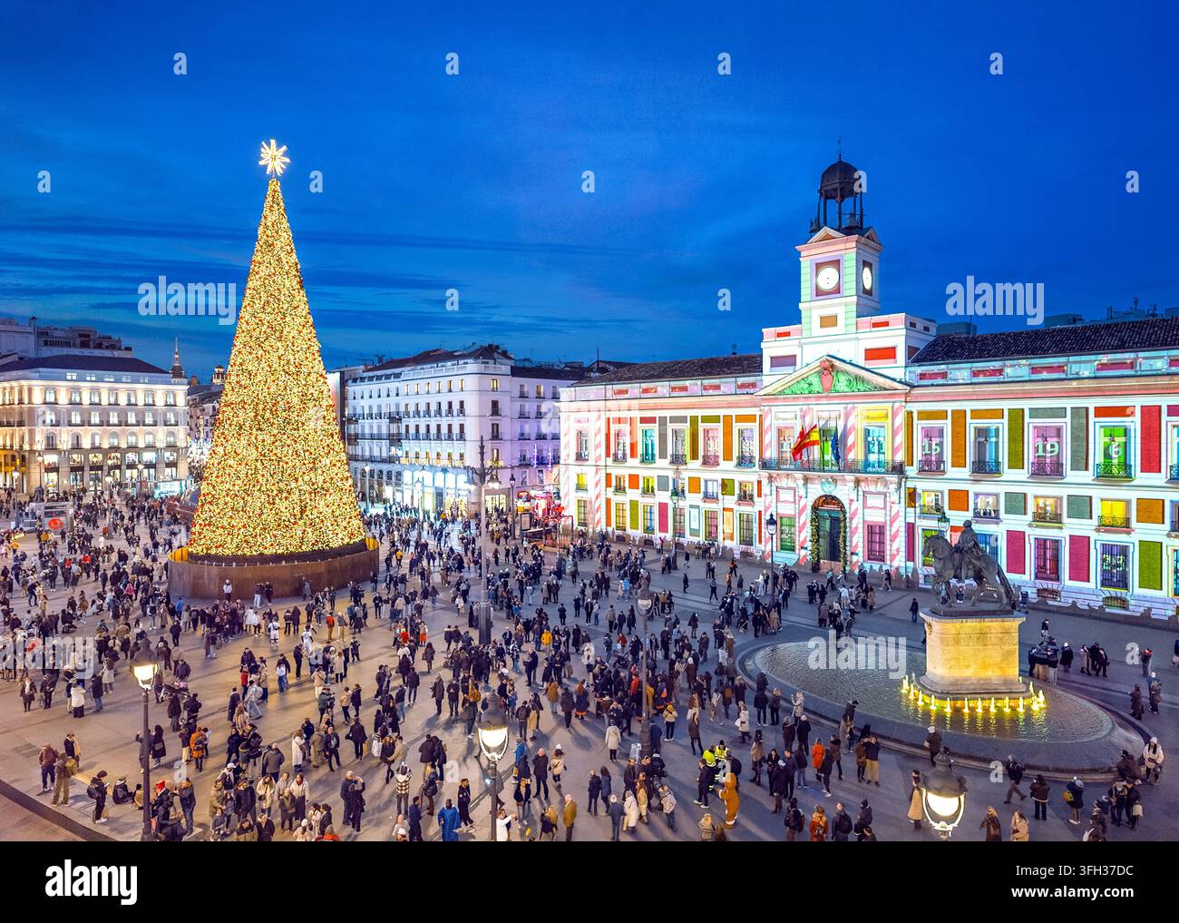 Un gigantesco albero di Natale illuminato in Piazza Puerta del Sol al crepuscolo, con l'iconico edificio della Real Casa de Correos. Madrid, Spagna. Foto Stock