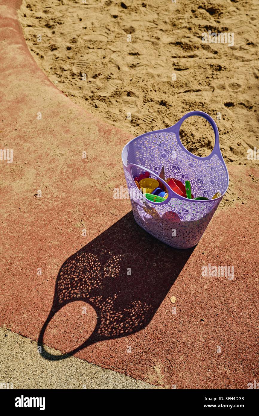 Cestino di plastica con giocattoli da sabbia in piedi sul bordo del parco giochi Foto Stock