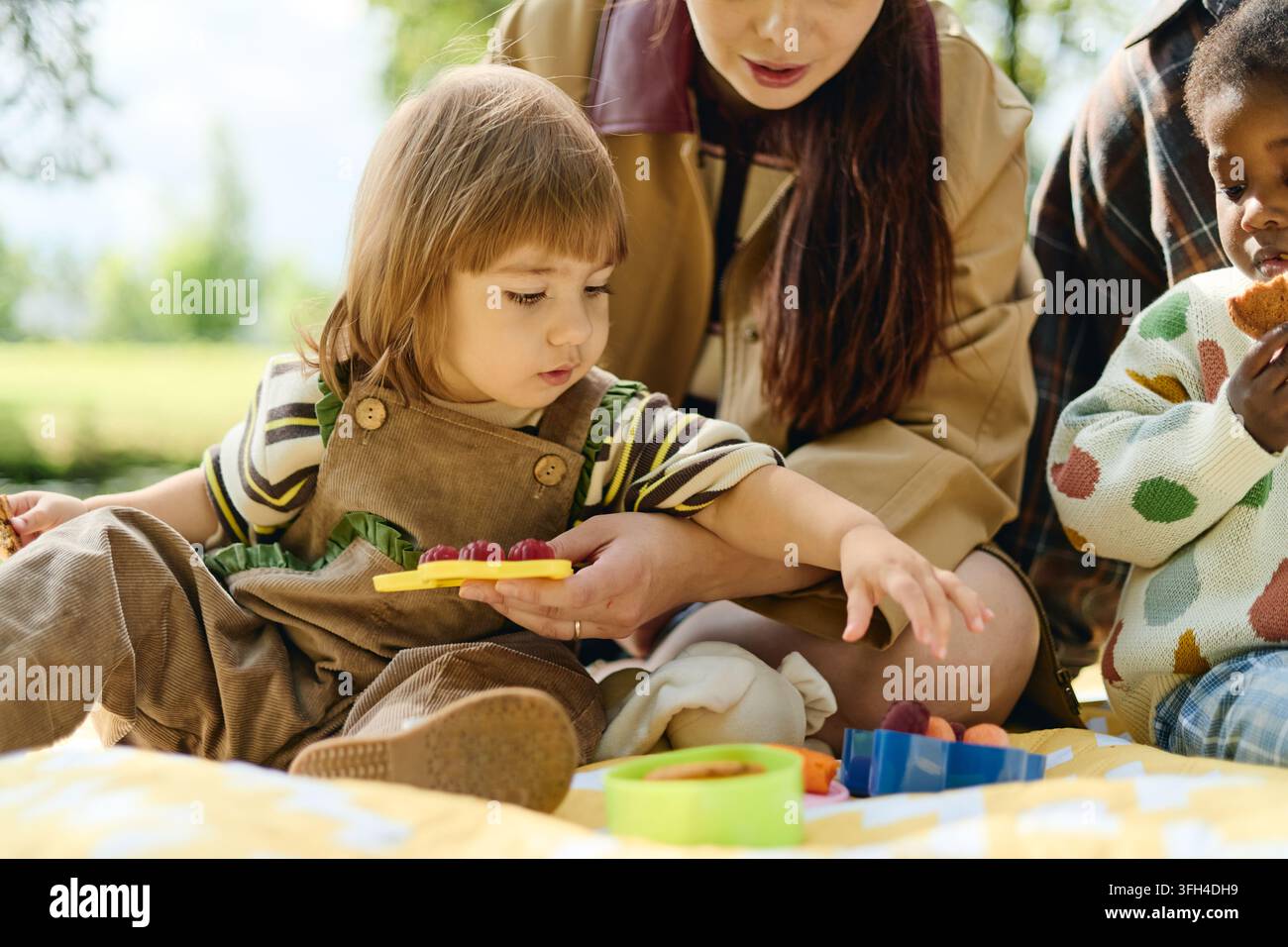 Madri diverse con bambini che gustano uno spuntino sano da picnic nel parco Foto Stock