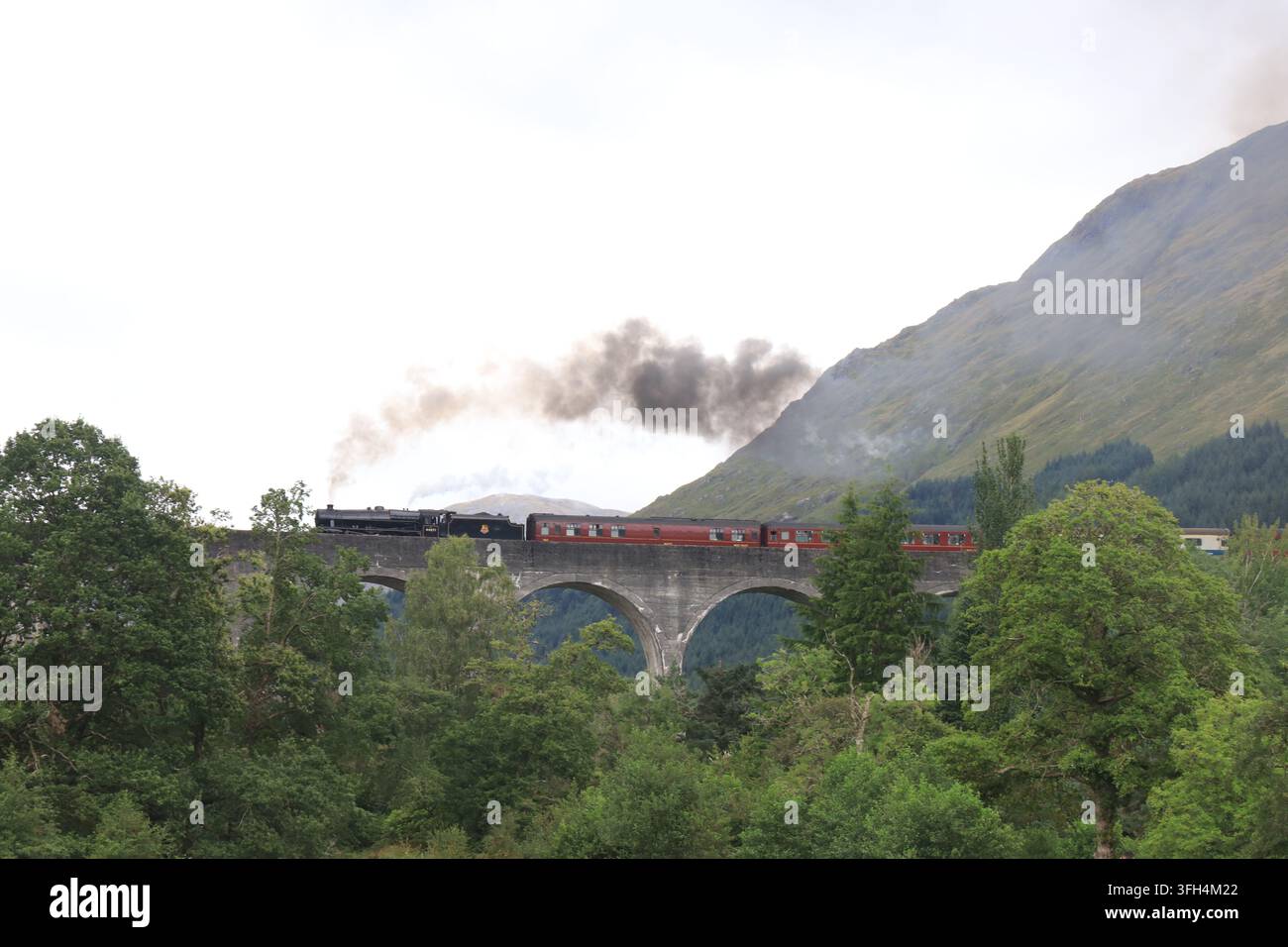 Il treno a vapore di Harry Potter emette fumo bianco e nero in mezzo a un paesaggio scozzese suggestivo. È diventato famoso dopo essere apparso nei film di Harry Potter. Foto Stock
