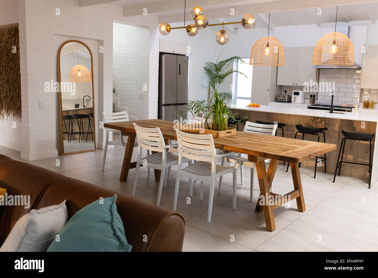 Un lungo tavolo da pranzo su cavalletti in legno ancorava l'area da pranzo open-plan con vaso e lampadario dorato Foto Stock