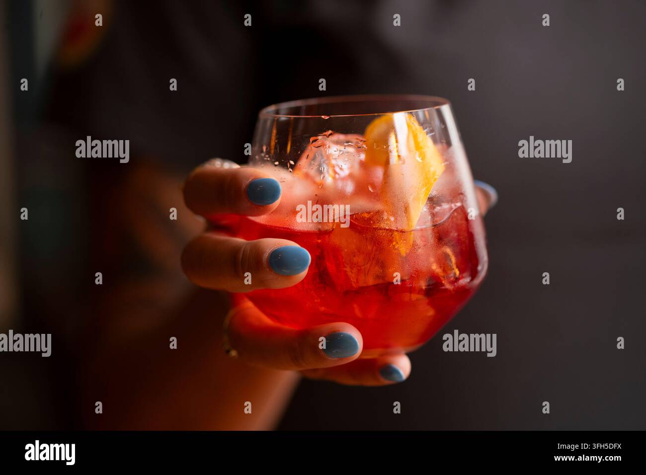 Un cocktail colorato con ghiaccio e fette di arancia viene sollevato, evocando la freschezza e la gioia estiva. Foto Stock
