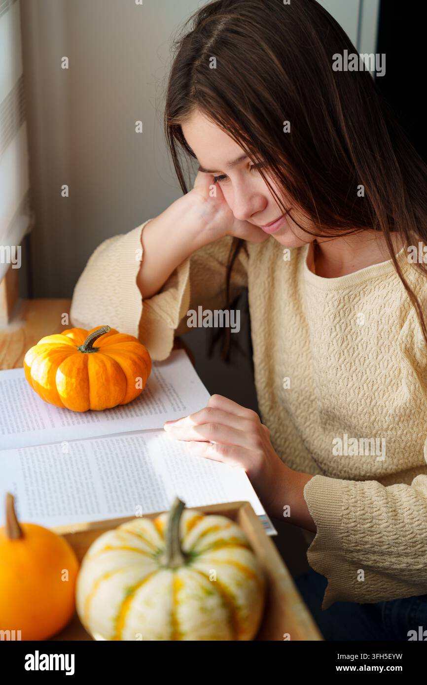 Ragazzina che legge un libro accanto a delle zucche nella calda luce autunnale Foto Stock