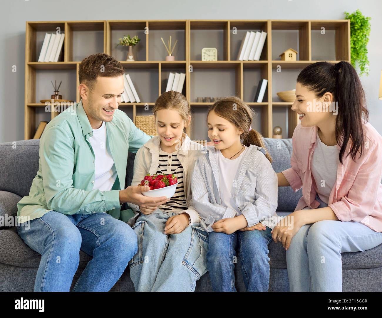 Famiglia felice con due figlie che mangiano fragole insieme sul divano a casa Foto Stock